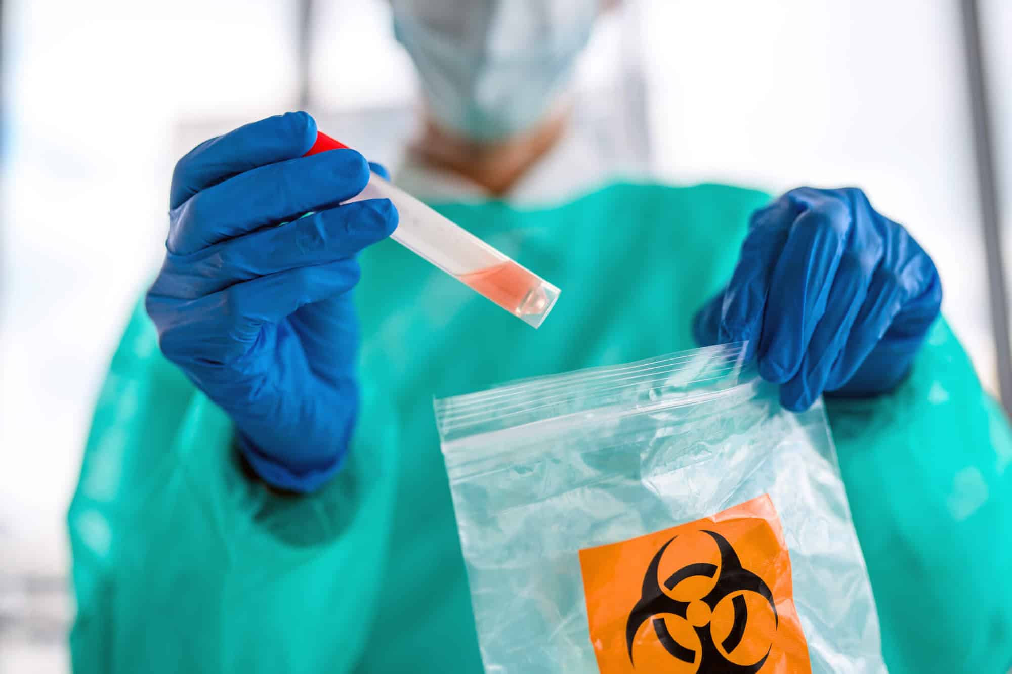 scientist placing a plastic test tube into a biohazard bag
