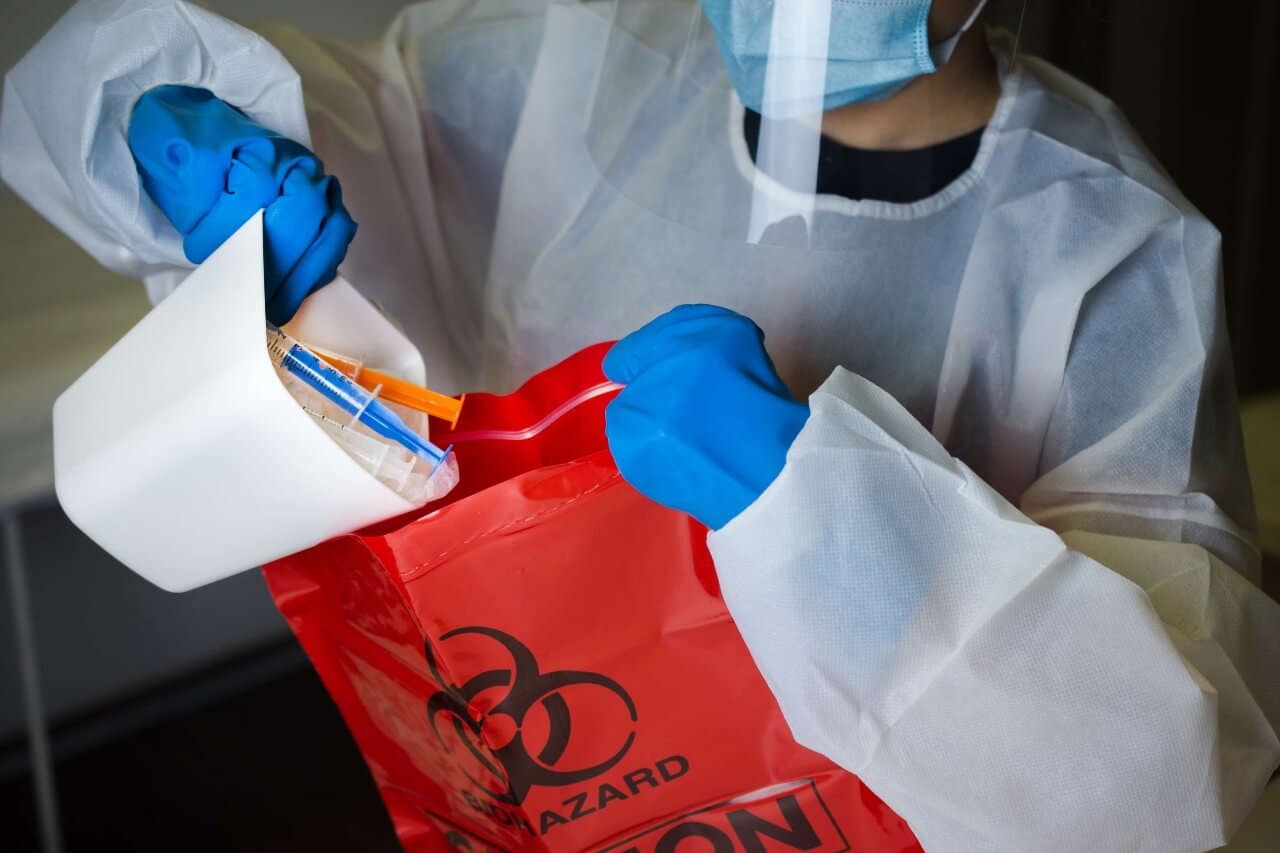 person wearing hazmat outfit dumps used needles into a red hazardous waste bag